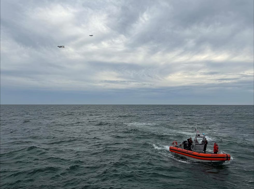 In this photo released by U.S. Coast Guard, crew members search by air and on the water for a...